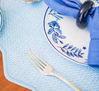 Detalhe da textura em rafia do jogo americano azul claro com prato de porcelana floral e guardanapo azul com porta-guardanapo