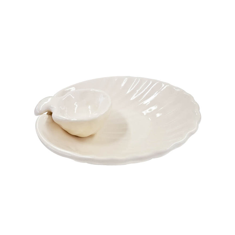 Petisqueira em formato de concha com molheira acoplada, feita de cerâmica artesanal na cor natural (off-white) com acabamento brilhante. A peça possui tamanho de 24 x 25 cm (concha) e 11 x 14 cm (molheira), com design autoral Lolahome produzido no Brasil, apresentando as variações charmosas de um produto feito à mão. Como deve ser usado: ideal para compor uma mesa posta de petiscos ou temática de mar, sendo perfeita para servir porções como camarões, iscas de peixe ou snacks acompanhados de molhos, patês