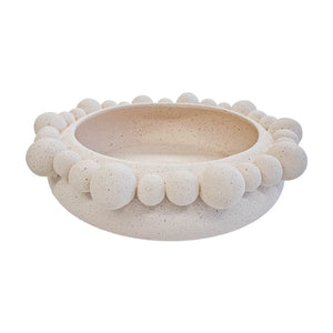 Centro de mesa redondo de cerâmica na cor marfim (natural), apresentando uma textura externa rica composta por diversas esferas em relevo. A peça possui tamanho de 35 cm de largura e 10 cm de altura, com design atemporal e acabamento rústico que destaca as variações únicas de cada peça. Como deve ser usado: ideal para compor a decoração de mesas de jantar ou centros de sala, sendo perfeito para acomodar frutas, esferas decorativas ou ser usado como uma peça de destaque chic e com personalidade.