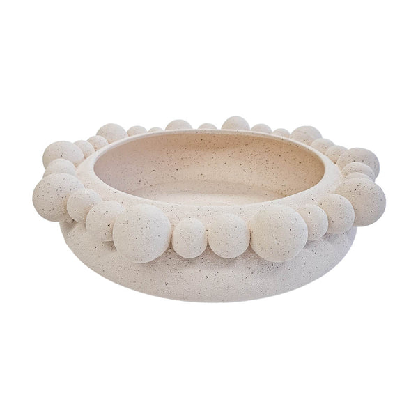 Centro de mesa redondo de cerâmica na cor marfim (natural), apresentando uma textura externa rica composta por diversas esferas em relevo. A peça possui tamanho de 35 cm de largura e 10 cm de altura, com design atemporal e acabamento rústico que destaca as variações únicas de cada peça. Como deve ser usado: ideal para compor a decoração de mesas de jantar ou centros de sala, sendo perfeito para acomodar frutas, esferas decorativas ou ser usado como uma peça de destaque chic e com personalidade.