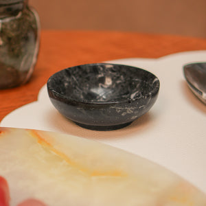 Bowl redondo pequeno de pedra natural ônix na cor preta, com acabamento polido e brilho intenso. A peça possui tamanho de 10 x 4 (h) cm, apresentando design atemporal e variações únicas de veios e texturas naturais, ideal para servir petiscos, molhos ou sobremesas na mesa posta