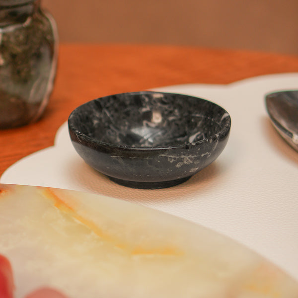 Bowl redondo pequeno de pedra natural ônix na cor preta, com acabamento polido e brilho intenso. A peça possui tamanho de 10 x 4 (h) cm, apresentando design atemporal e variações únicas de veios e texturas naturais, ideal para servir petiscos, molhos ou sobremesas na mesa posta